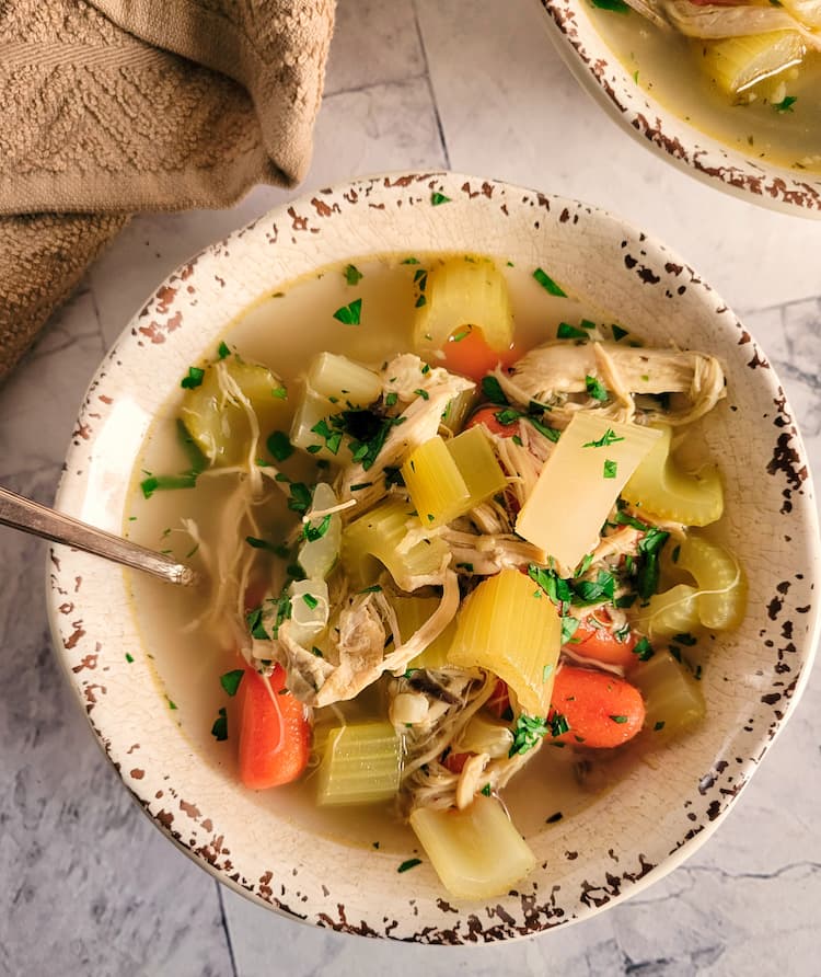 bowl of no noodle chicken soup with chopped parsley, baby carrots, celery and shredded chicken