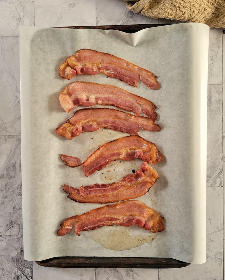 parchment lined baking sheet with 6 slices of cooked bacon