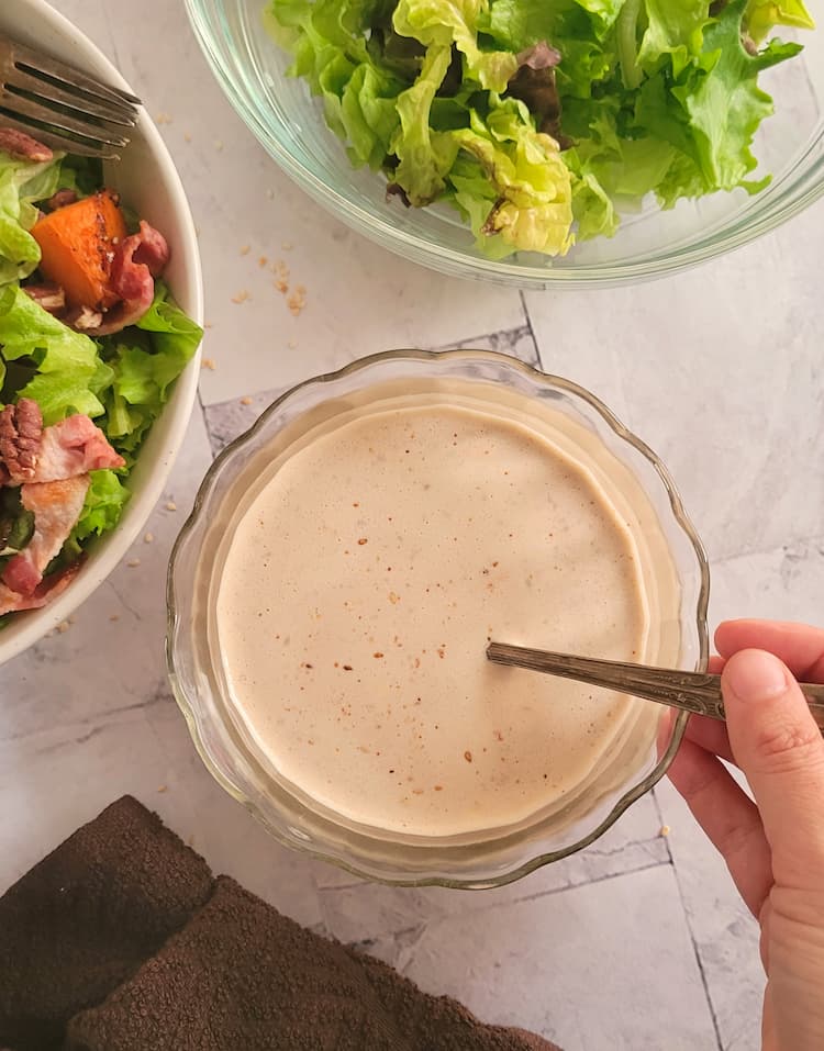 bowl of creamy/yellow sauce with a spoon in it, hand on the spoon, salads in the background