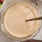 bowl of creamy/yellow sauce with a spoon in it, salads in the background
