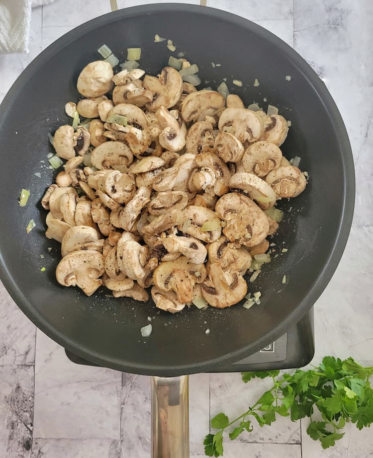 wok with uncooked sliced white mushrooms, diced white onion and minced garlic