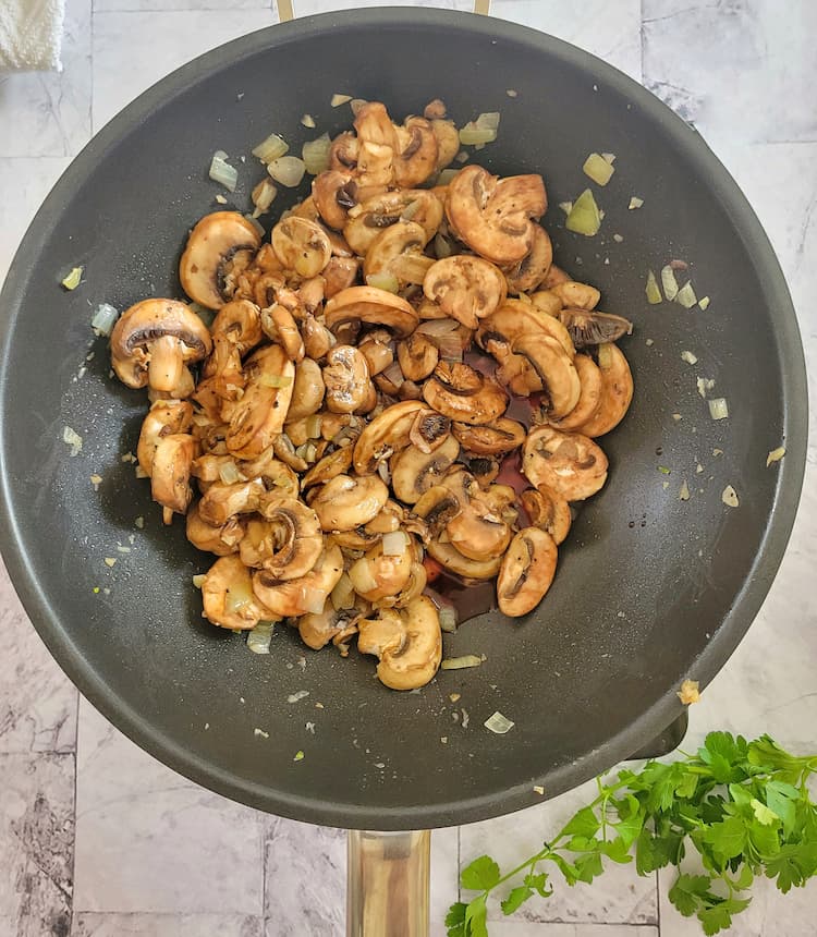 wok with cooked sliced mushrooms, minced garlic and diced white onions