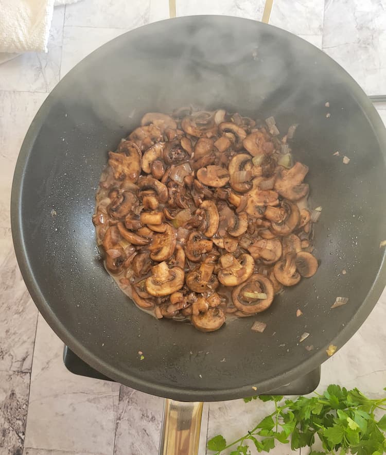 smoking hot wok with sliced mushrooms in liquid