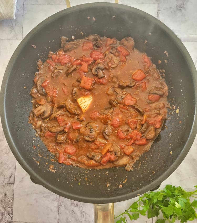 wok with diced tomatoes, sliced mushrooms and a parmesan rind
