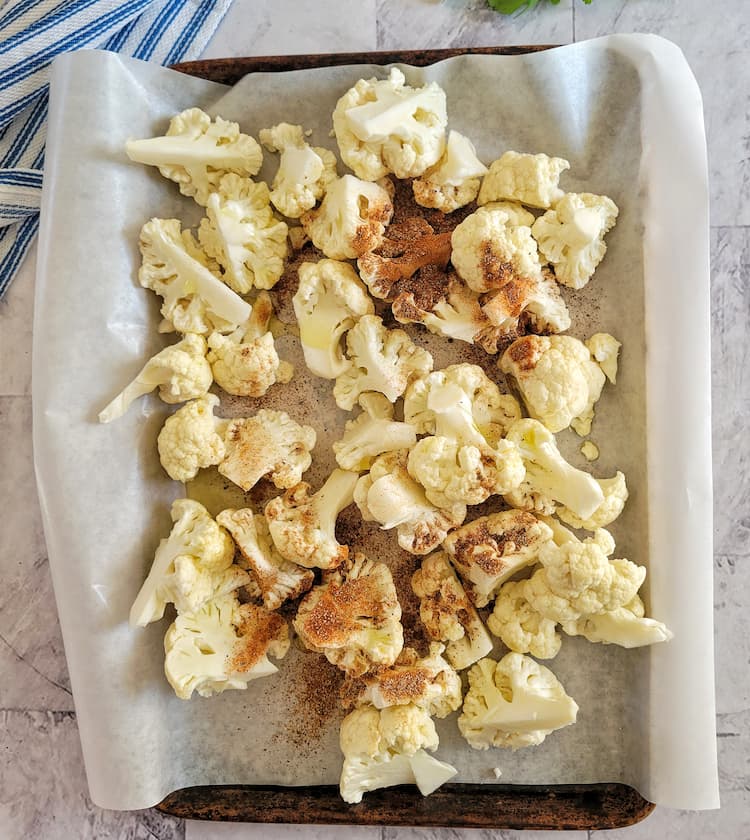 parchment lined sheet pan with raw cauliflower florets with oil and spices