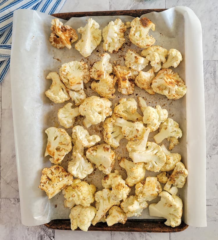 parchment lined baking sheet with raw and seasoned cauliflower florets