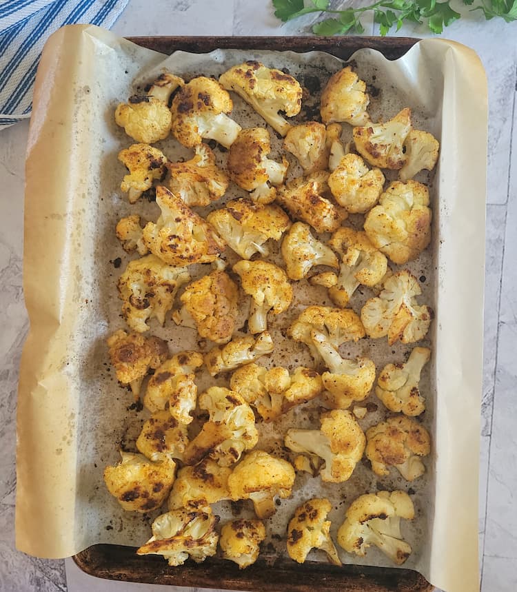 parchment lined sheet pan with seasoned and roasted cauliflower florets