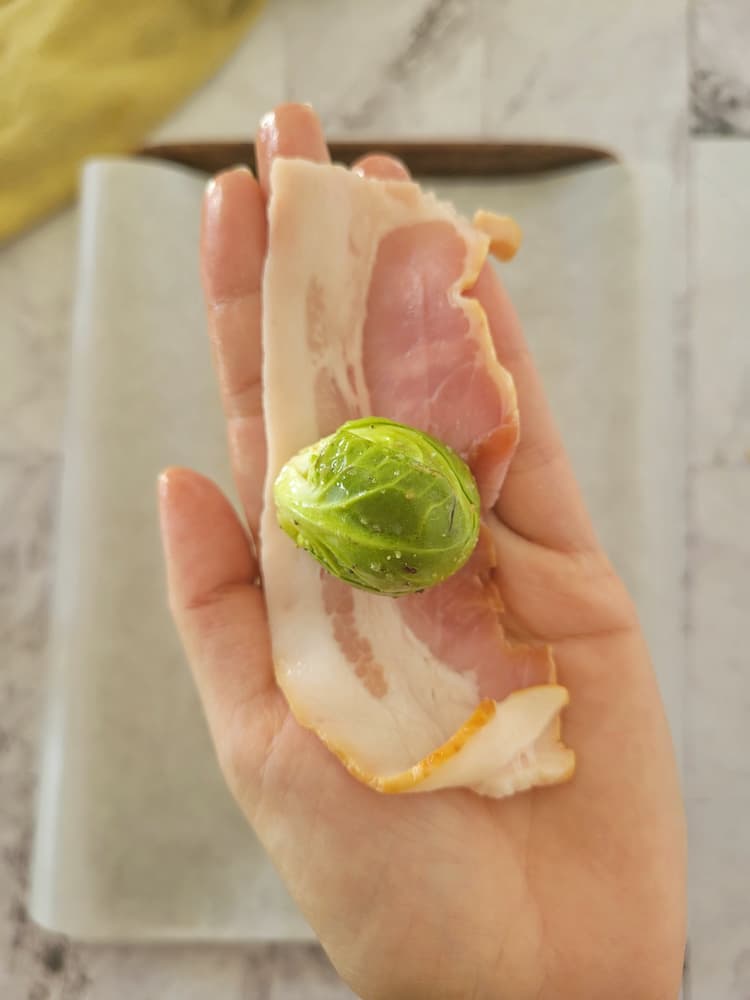 hand holding a half piece of bacon with a whole brussels sprout in the middle