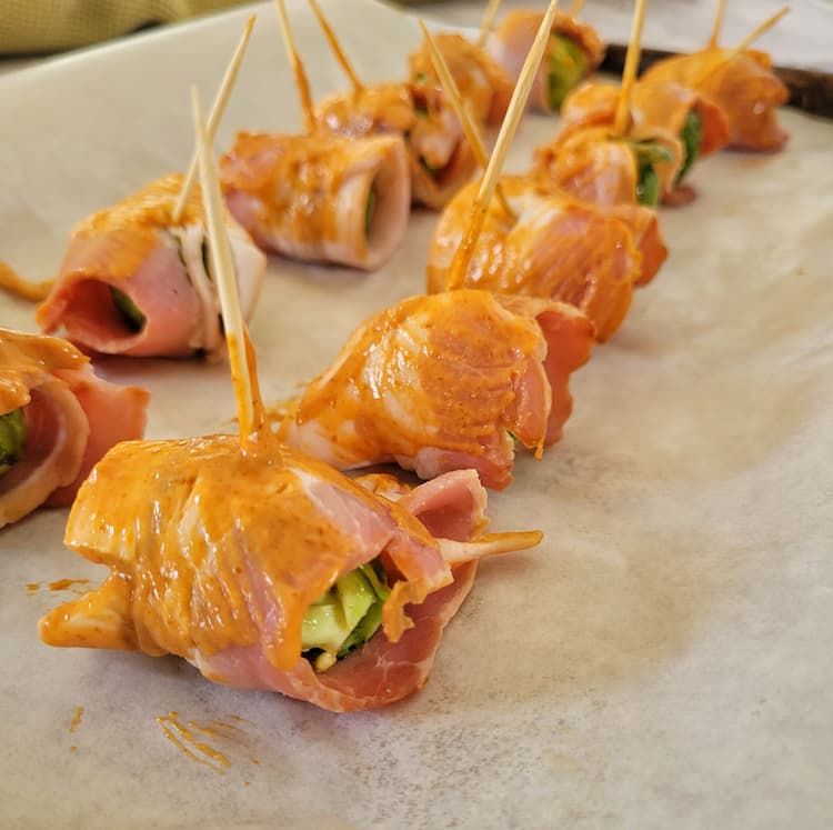 raw bacon wrapped brussels sprouts with an orange glaze and toothpicks on a parchment lined baking sheet