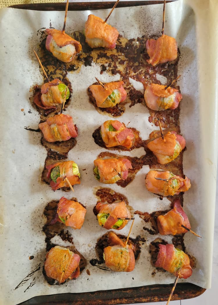 parchment lined baking sheet with cooked bacon wrapped brussels sprouts, toothpicks in each