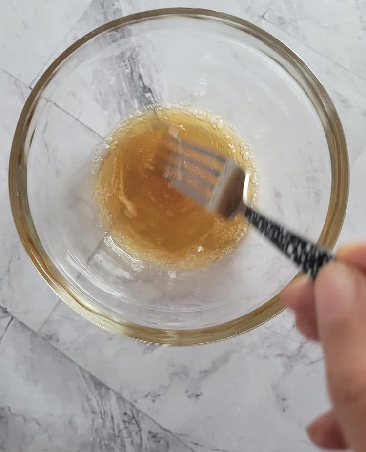 hand with a fork whisking a bowl of frothy brown liquid