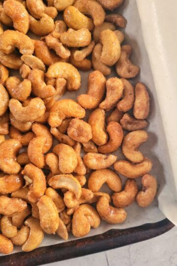 close up of a parchment lined baking sheet full of candied cashews