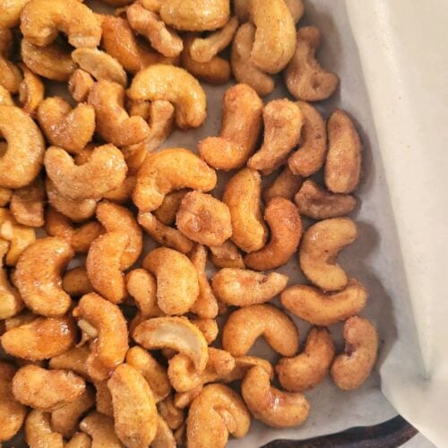 close up of a parchment lined baking sheet full of candied cashews.
