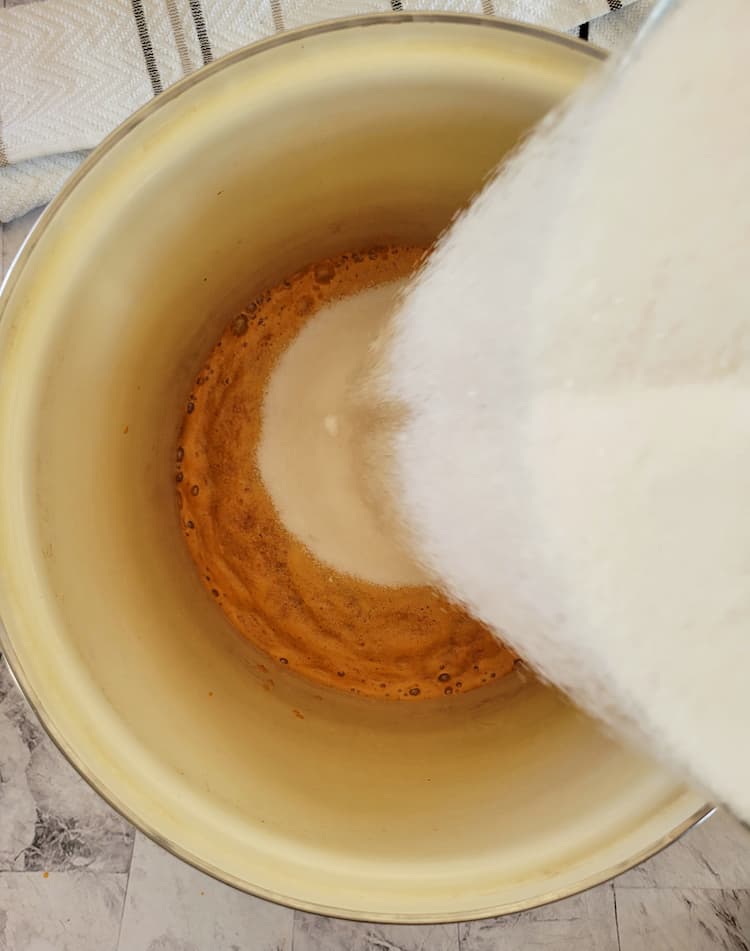 sugar being poured into a pot with orange foam/liquid