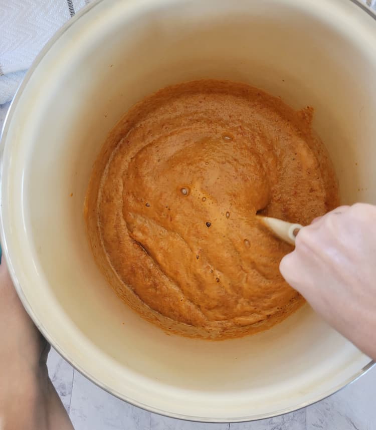 hand stirring a large pot of orange foamy liquid