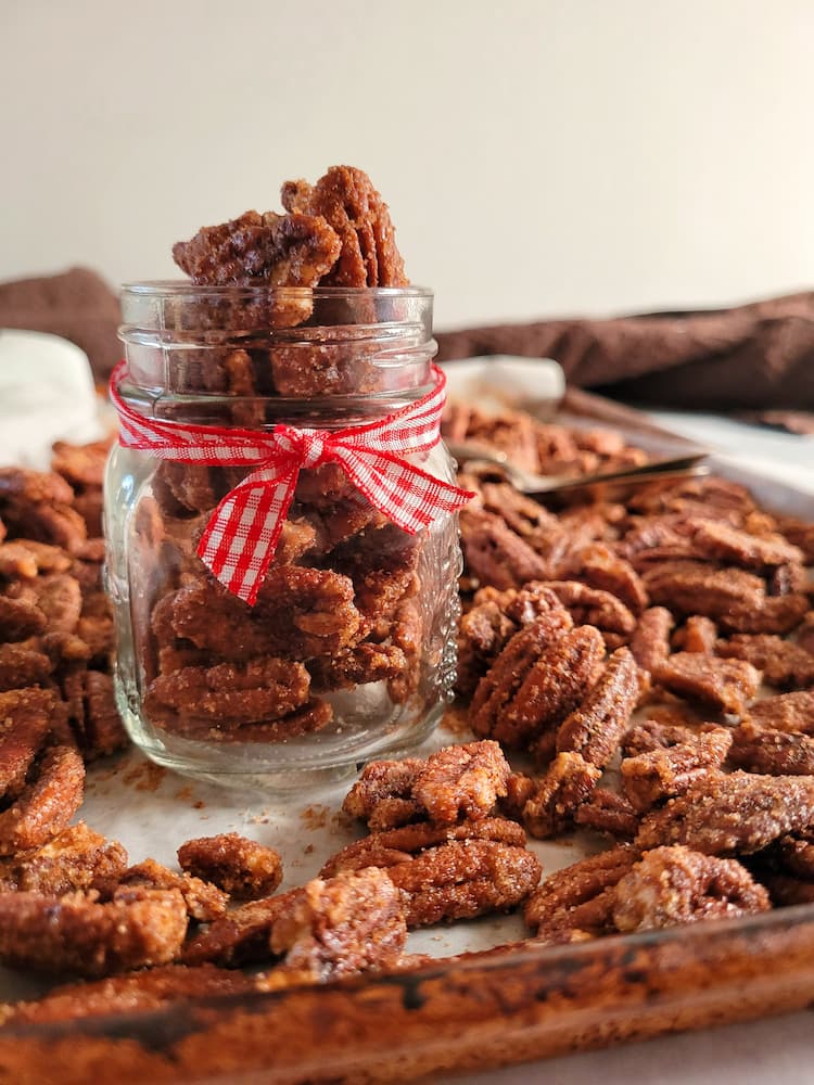 small jar with a ribbon holding candied pecans on a tray with the rest