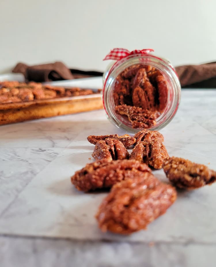 jar tipped over with spiced candied pecans coming out, more on a tray in the background
