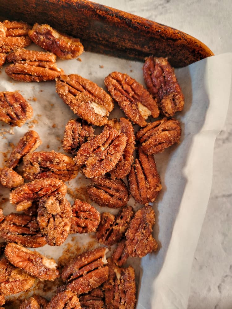 corner of a parchment lined baking sheet with candied pecans