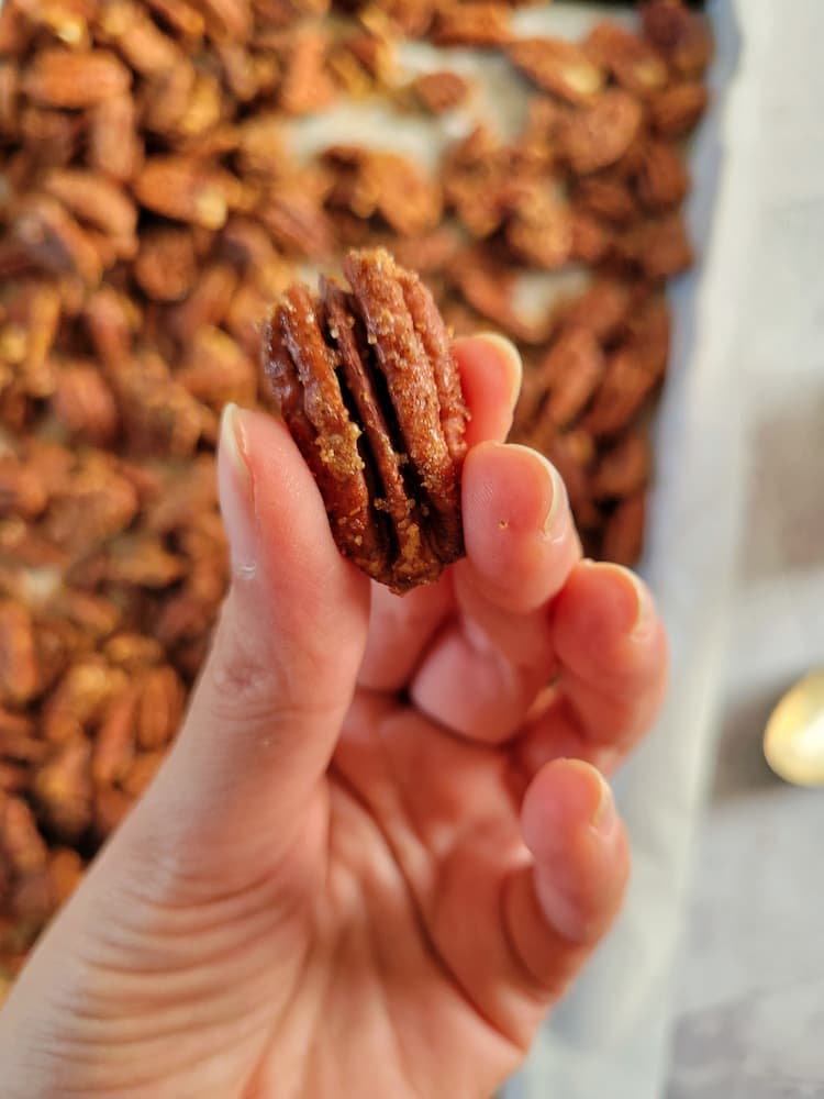 hand holding up a spiced candied pecan above a tray with the rest