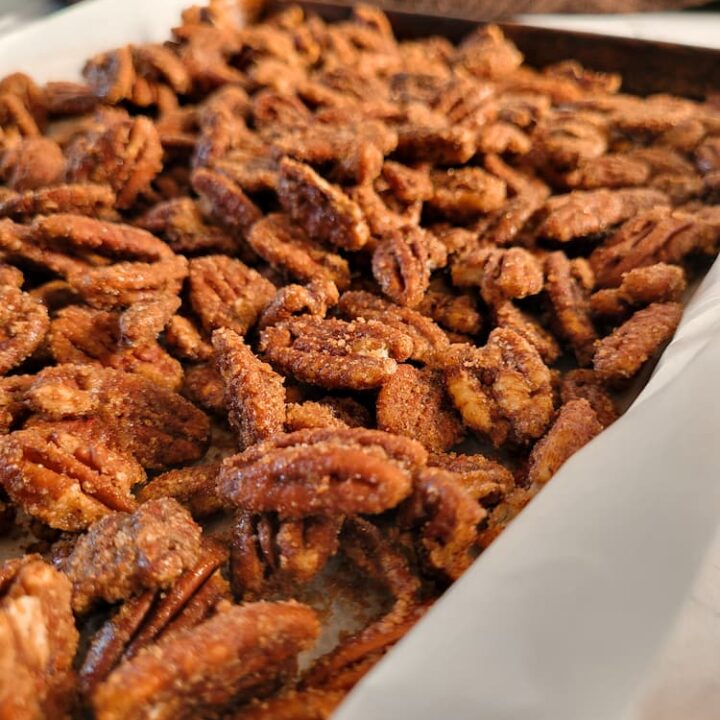 side view of spiced candied pecans on a parchment lined baking sheet