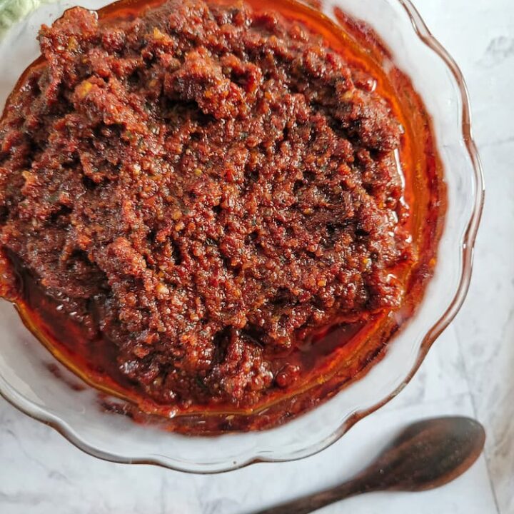 bowl of sun-dried tomato pesto, hand touching a wooden spoon in the background