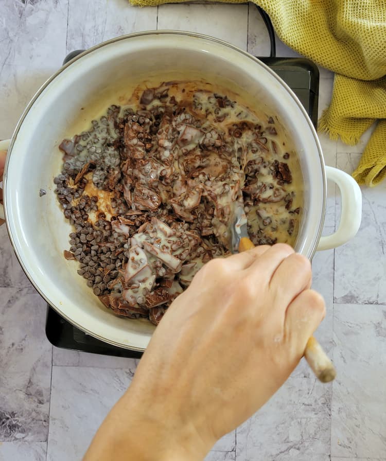 hand with a rubber spatula in a pot stirring chocolate chips and condensed milk