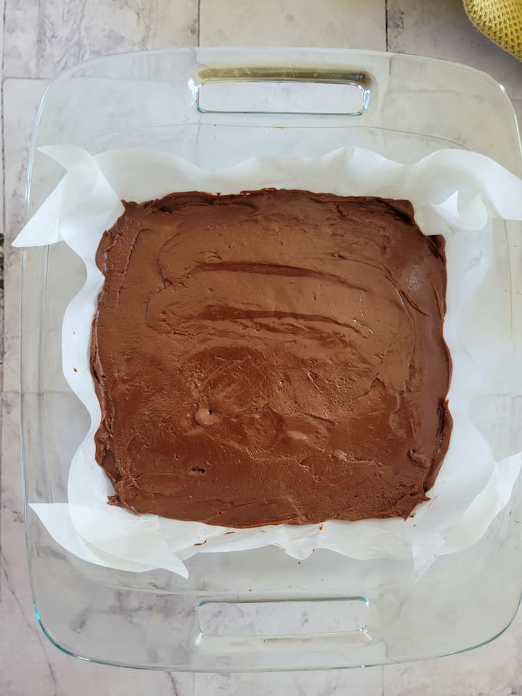 square glass baking dish lined with parchment paper and chocolate batter