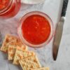 two jars of red pepper jelly with 5 saltine crackers and a knife