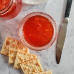 two jars of red pepper jelly with 5 saltine crackers and a knife