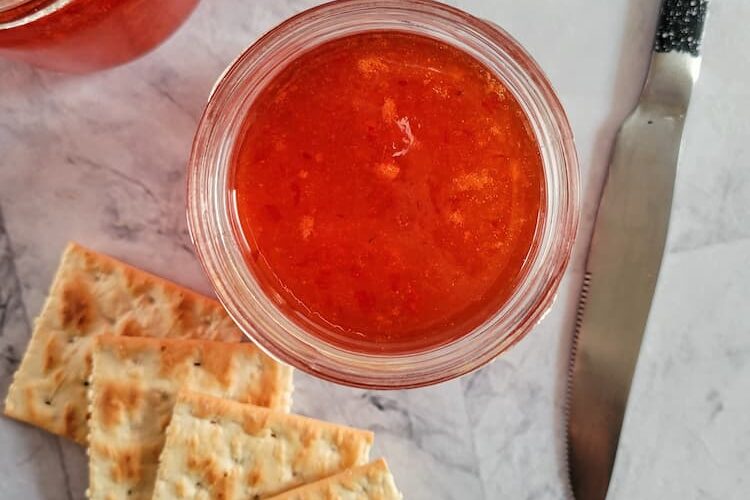 two jars of red pepper jelly with 5 saltine crackers and a knife
