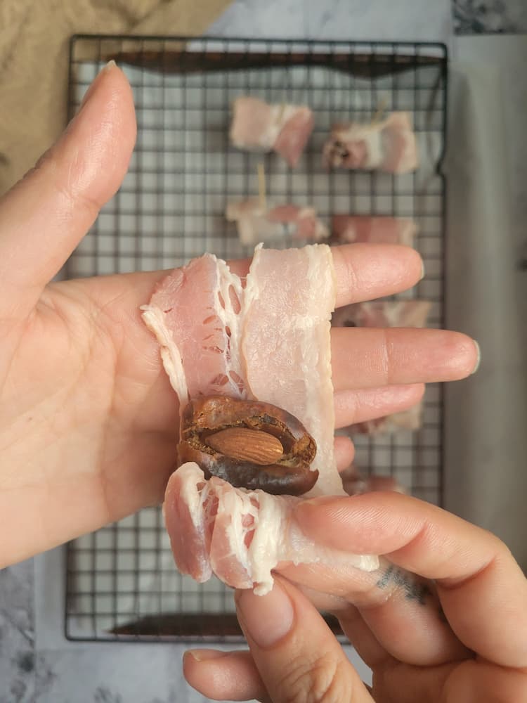almond stuffed date being wrapped in a piece of raw bacon over a tray of the rest