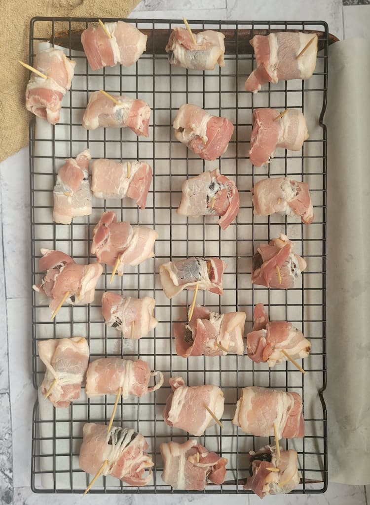 wire rack over a parchment lined baking sheet with raw bacon wrapped dates