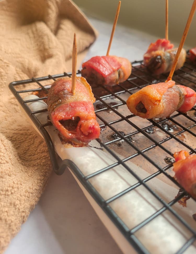 cooked bacon wrapped dates pricked with toothpicks on a wire rack with parchment paper