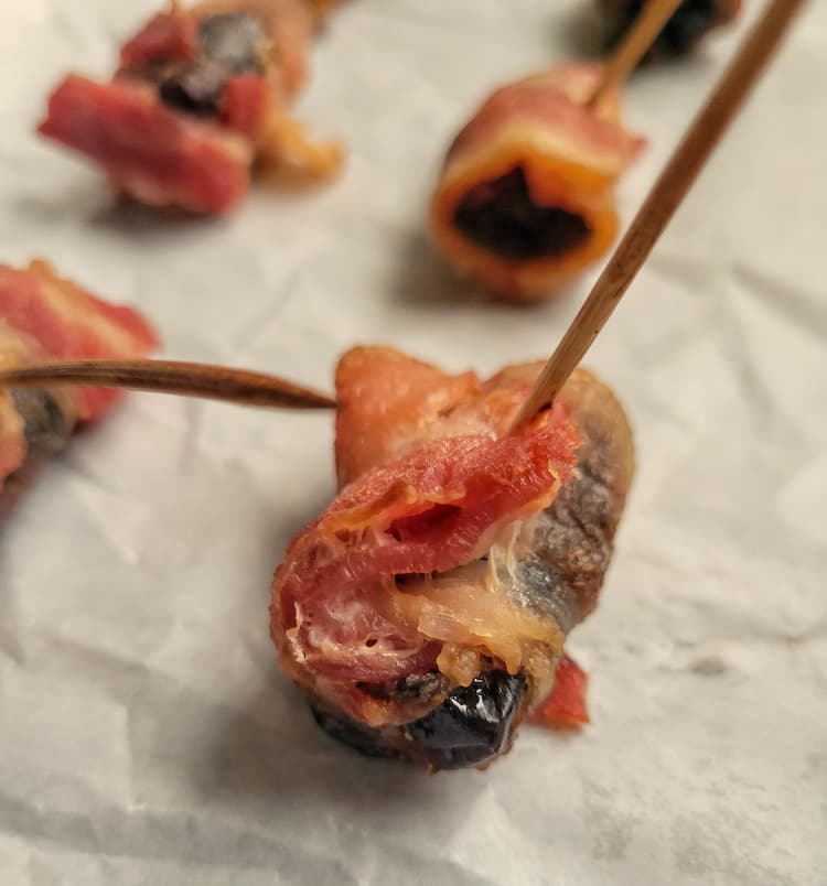close up of a bacon wrapped date on a piece of parchment paper, more in the background