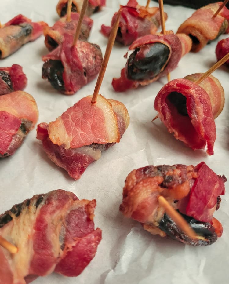 cooked bacon wrapped dates with toothpicks on parchment paper