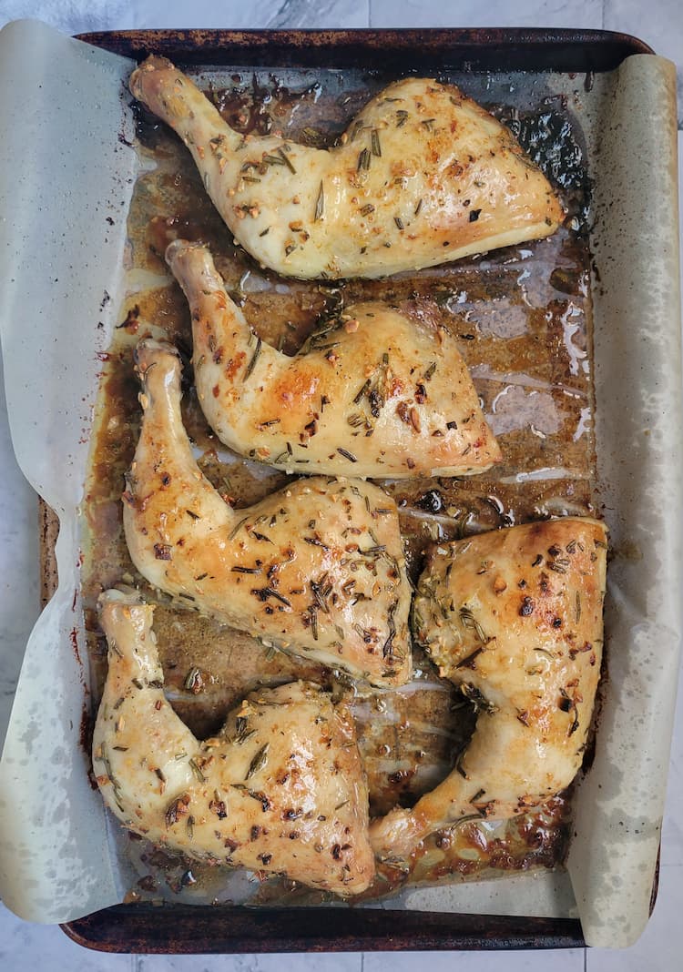 roasted rosemary and garlic chicken leg quarters on a parchment lined baking sheet