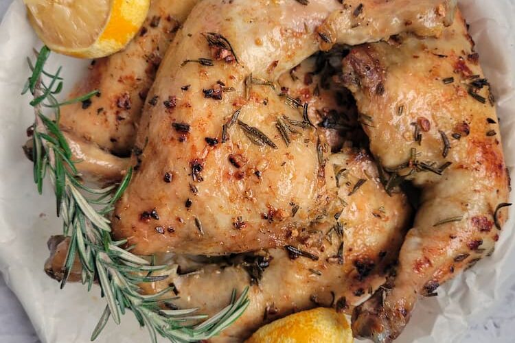 roasted chicken leg quarters with fresh sprigs of rosemary and lemon halves on a parchment lined circular tray