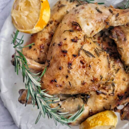 roasted chicken leg quarters with fresh sprigs of rosemary and lemon halves on a parchment lined circular tray