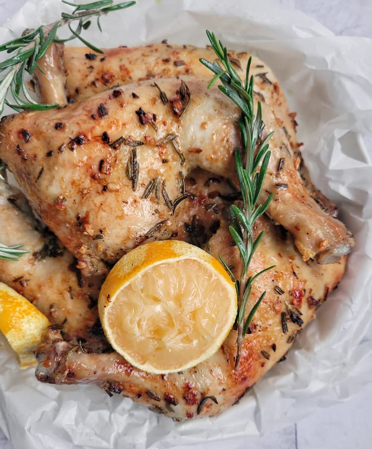 roasted chicken legs quarters with fresh sprigs of rosemary and lemon halves