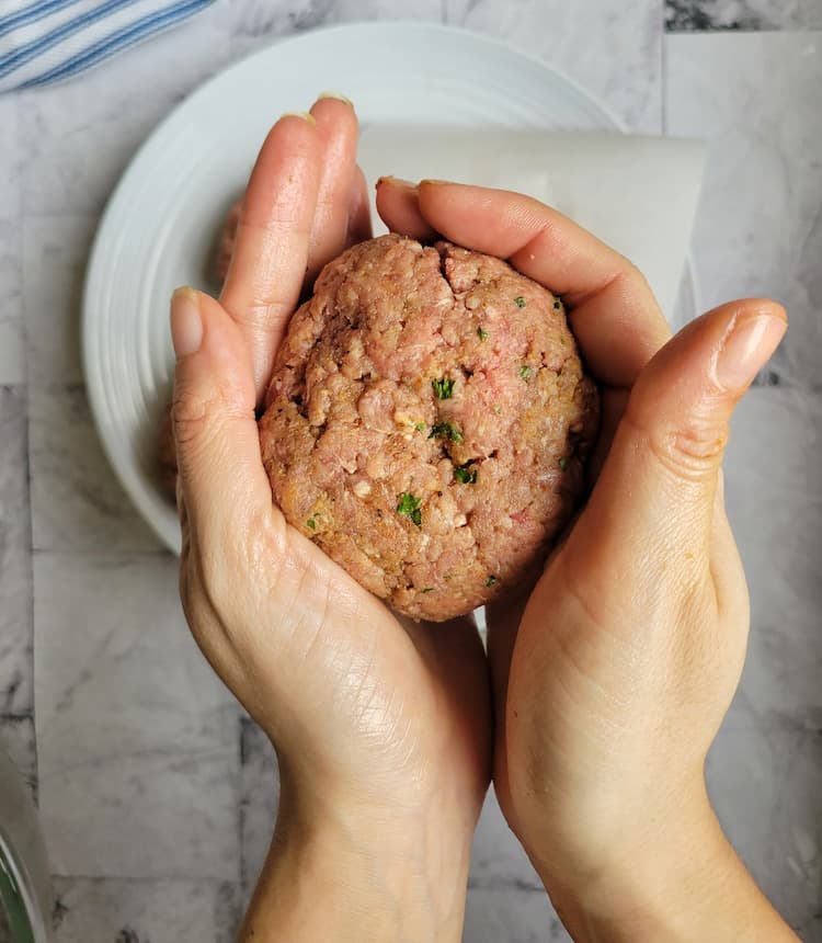hands smoothing out the edges of a big meatball