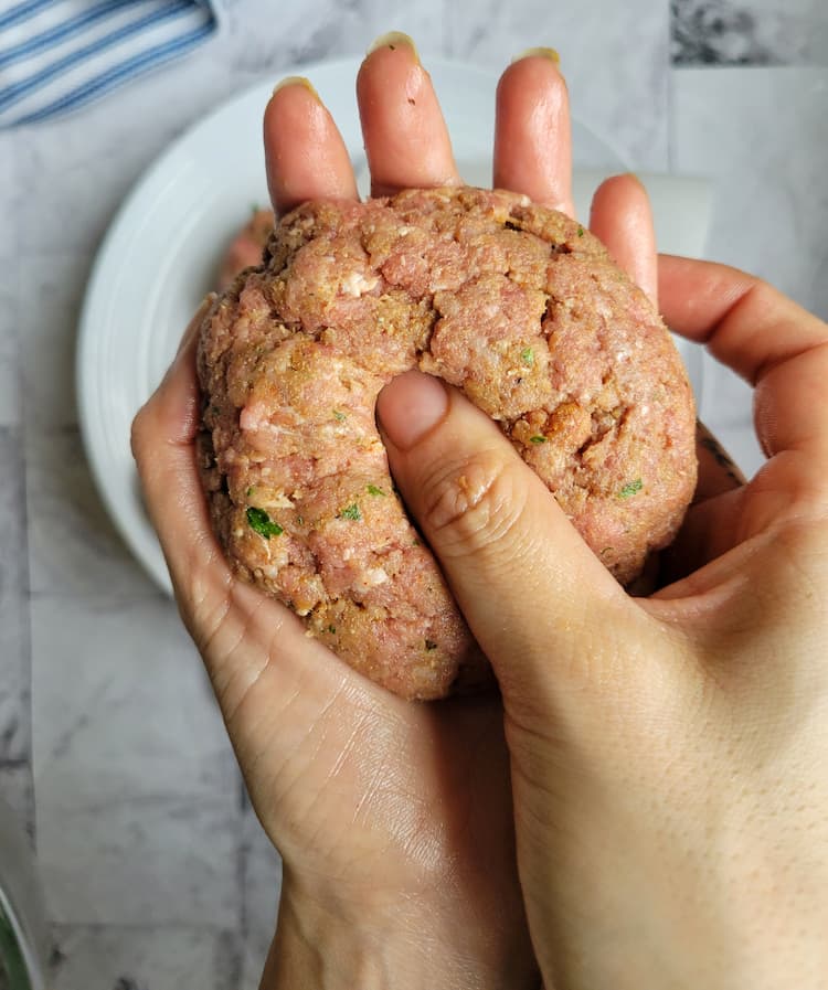 raw hamburger patty in the palm of a hand making a thumprint in the center