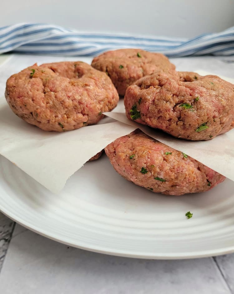 4 raw ground beef patties stacked between parchment paper on a plate