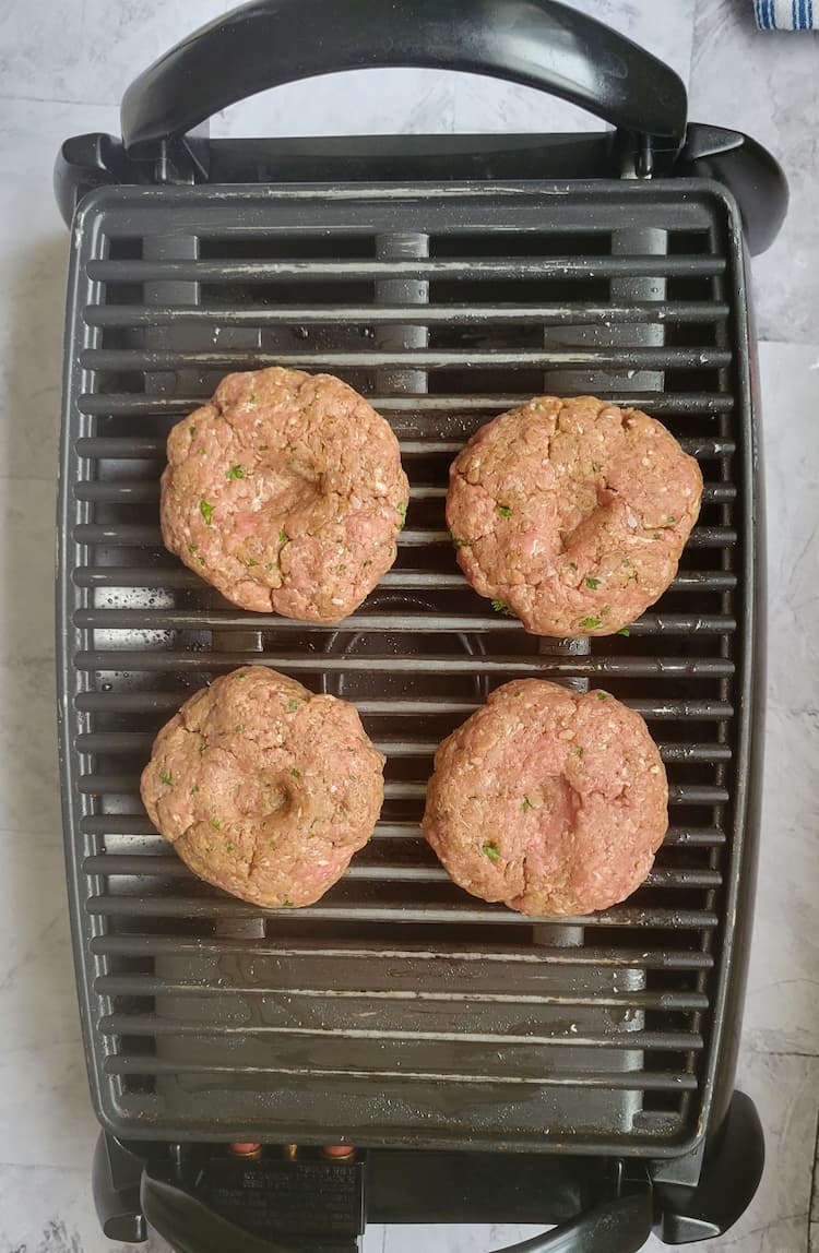 4 raw hamburger patties with indents on an indoor grill