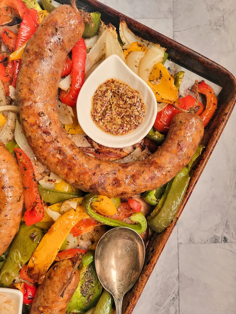 whole grainy mustard in a ramekin on a sheet pan with sausage with pepper and onions, spoon on the pan