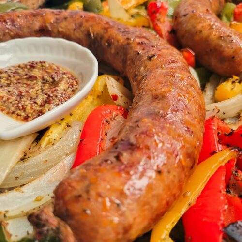 close up of an italian sausage next to some grainy mustard, on top of cooked onions and peppers