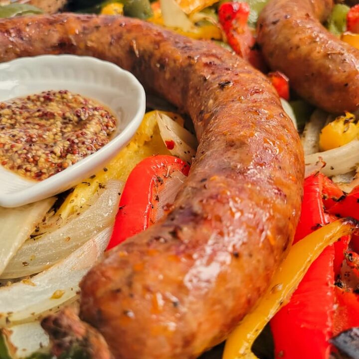 close up of an italian sausage next to some grainy mustard, on top of cooked onions and peppers