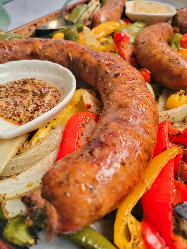 close up of an italian sausage next to some grainy mustard, on top of cooked onions and peppers