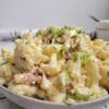 cauliflower 'potato' salad in a bowl with a creamy sauce, celery pieces, bacon, onions and fresh chopped parsley