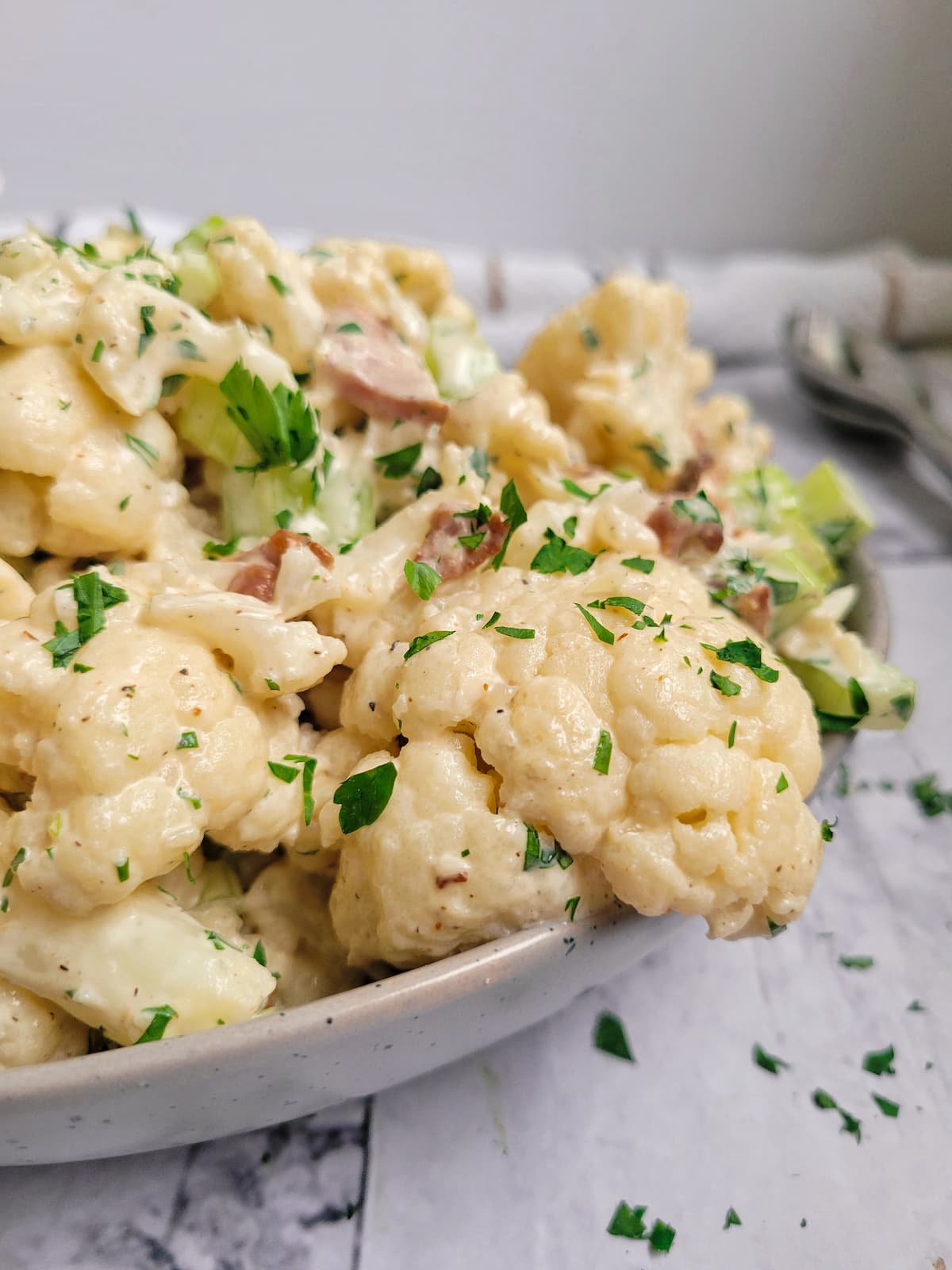side view of cauliflower florets in a bowl with bacon, celery and fresh chopped parsley in a creamy sauce