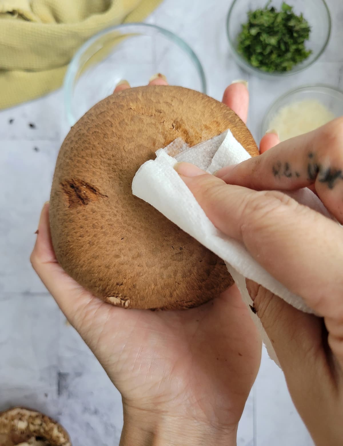 hand with a paper towel wiping the back of a portobello mushroom clean